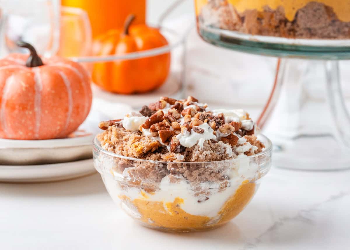 Serving of pumpkin cheesecake trifle in a small glass bowl topped with whipped cream and chopped pecans.