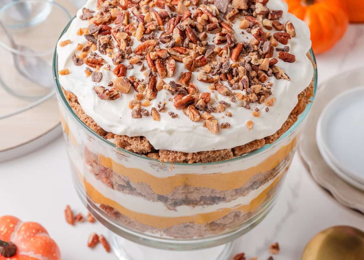 This pumpkin trifle is easy to make with layers of spice cake, creamy pumpkin cheesecake and whipped cream. It's an impressive fall dessert to serve a crowd! Top view of Thanksgiving pumpkin trifle topped with whipped cream, chopped pecans, and toffee bits.