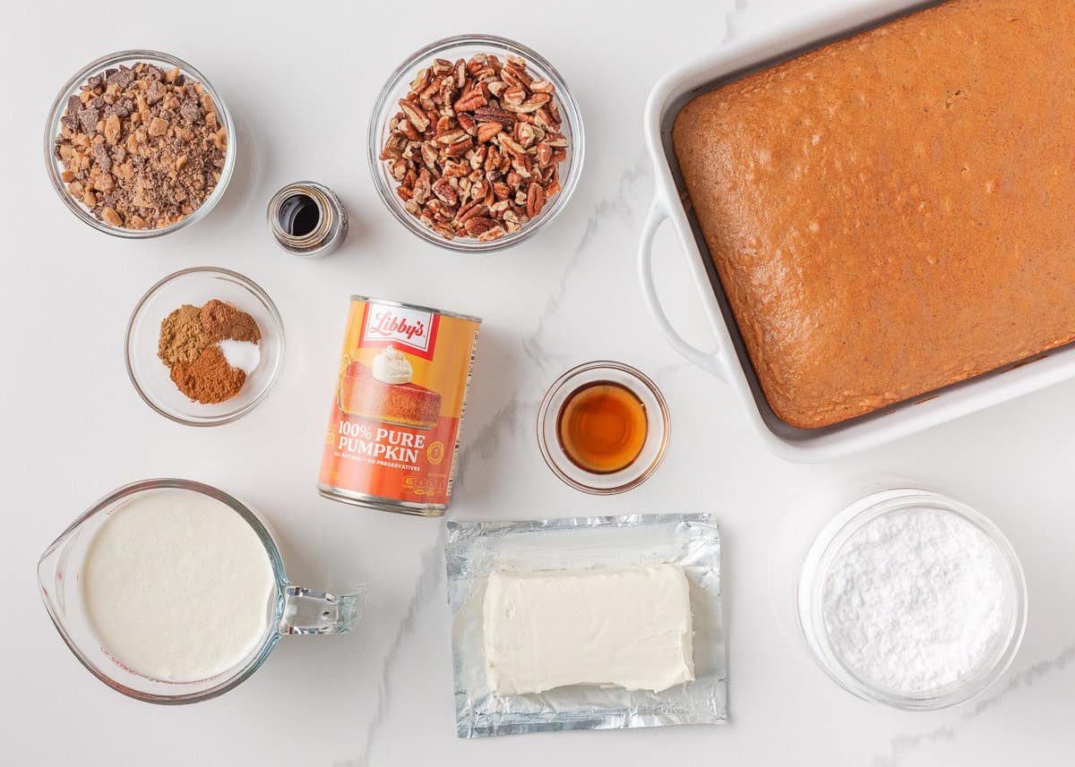 Pumpkin trifle ingredients including canned pumpkin, cream cheese, whipped cream, powdered sugar, spices, pecans, toffee bits, and baked spice cake.