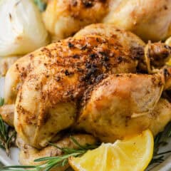 Close-up of baked cornish hens with crispy seasoned skin, garnished with lemon wedges and rosemary.