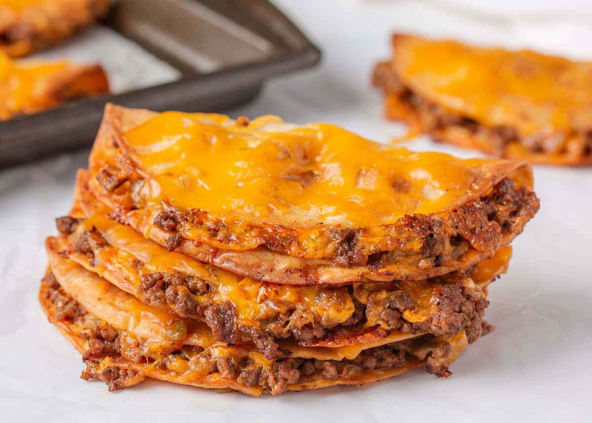 Close-up of crispy sheet pan tacos filled with seasoned beef and topped with melted cheddar cheese on a parchment-lined baking sheet.
