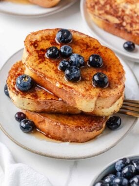 Stack of sourdough French toast slices topped with blueberries and maple syrup on a white plate.