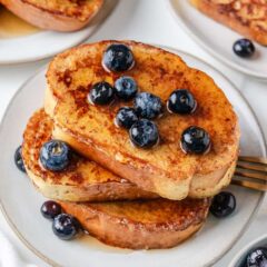 Golden sourdough French toast with fresh blueberries and syrup served on a plate.