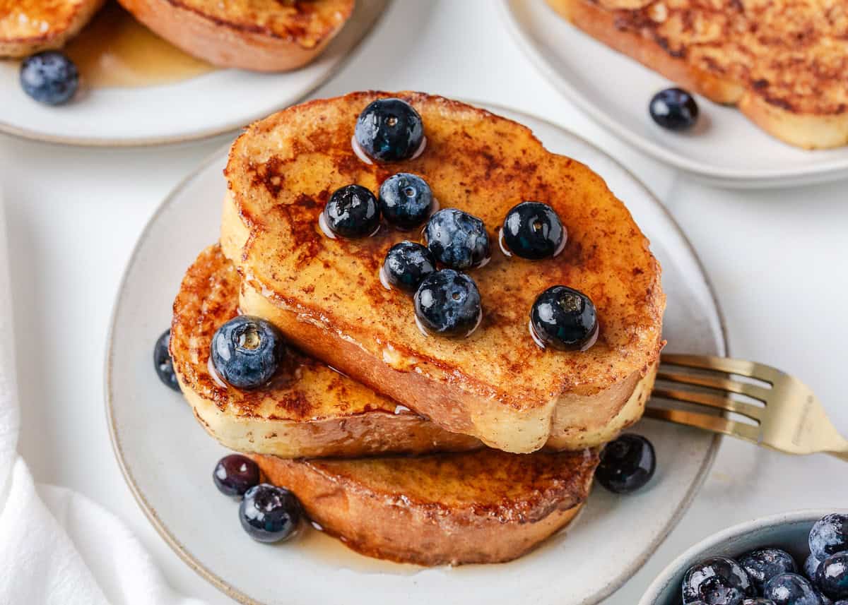 Golden sourdough French toast with fresh blueberries and syrup served on a plate.