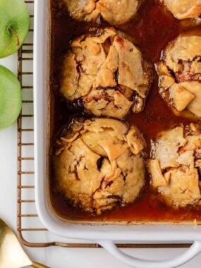 Freshly baked apple dumplings in a white casserole dish, bubbling in a cinnamon brown sugar sauce.