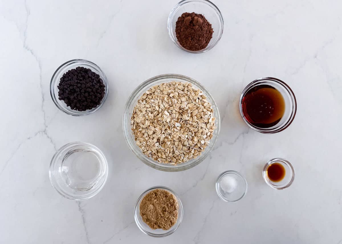 Chocolate granola ingredients including oats, brown sugar, cocoa powder, maple syrup, coconut oil and chocolate chips.