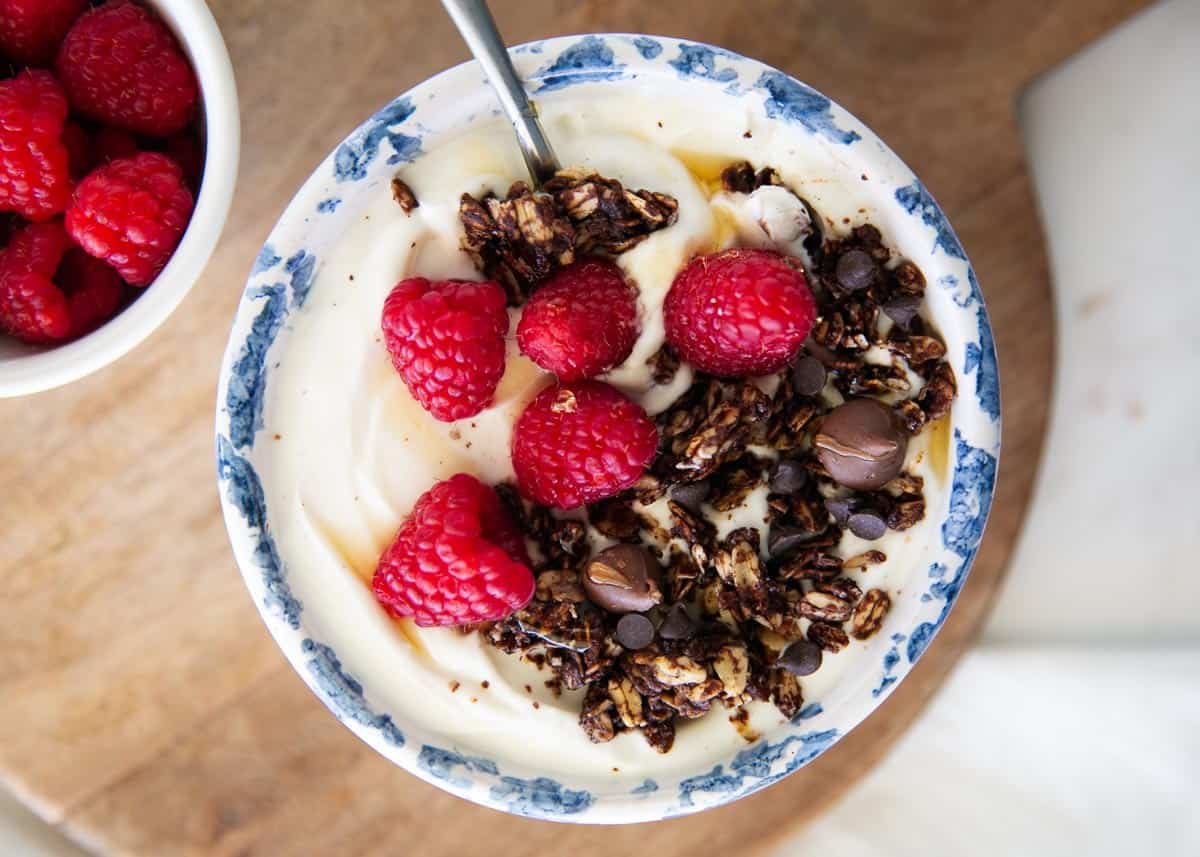Chocolate granola and yogurt in a decorative bowl topped with fresh raspberries. 