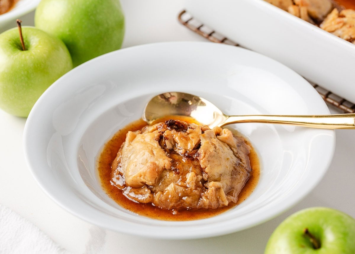 Single serving of old fashioned apple dumpling in a white bowl with golden syrup, ready to eat with a spoon.