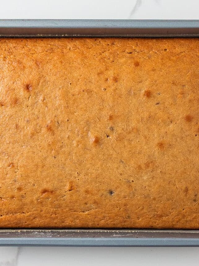 Freshly baked banana cake in a pan with a golden-brown top, showing a soft and moist texture.