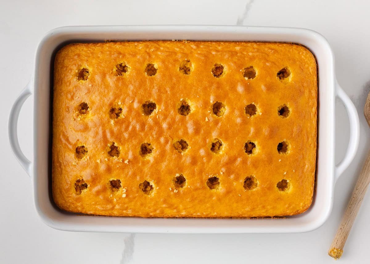 Yellow cake baked in a white pan with holes poked across the top for Boston cream pudding filling.