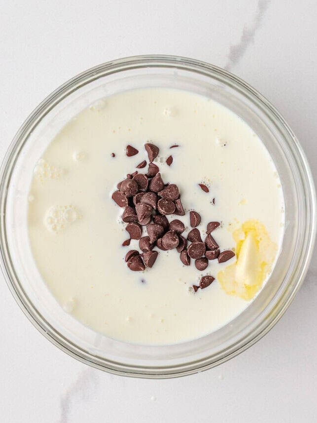 Ingredients for chocolate ganache including milk, butter, and chocolate chips in a glass bowl.