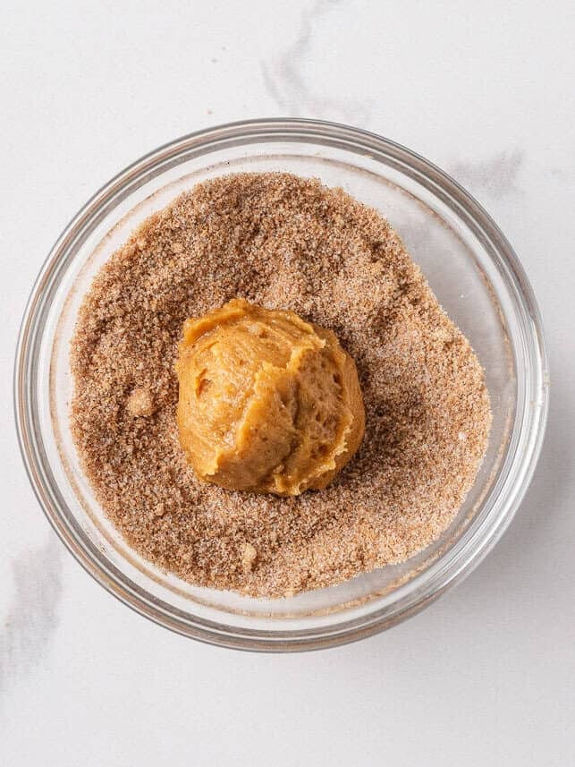 Perfectly spiced and deliciously sweet with the nutty aroma of brown butter, these chewy brown butter pumpkin cookies deliver all the fall coziness in every bite! Pumpkin cookie dough ball coated in cinnamon sugar, ready to be baked for chewy pumpkin cookies.