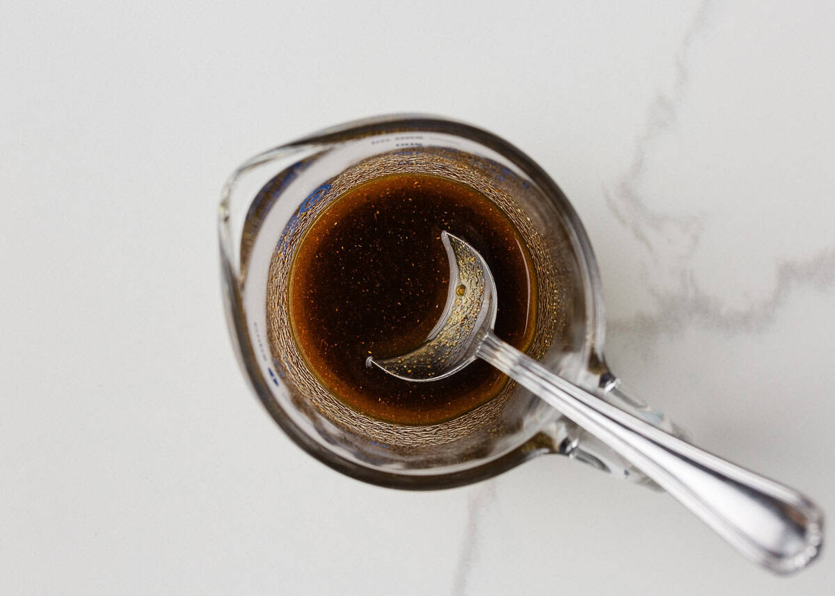 Homemade marinade of olive oil, garlic, and spices mixed in a glass measuring cup.