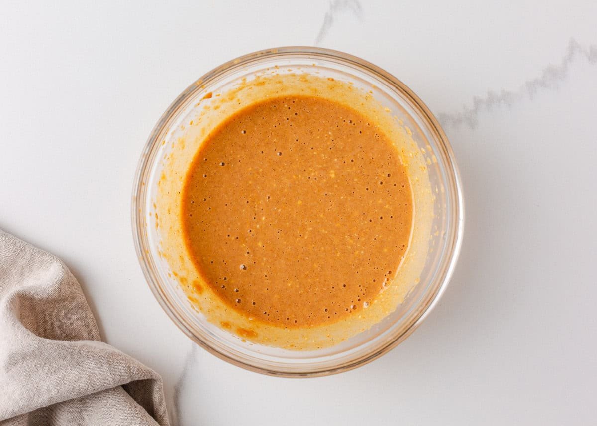 Smooth pumpkin cheesecake batter in a glass mixing bowl, ready to be layered over brownie batter.