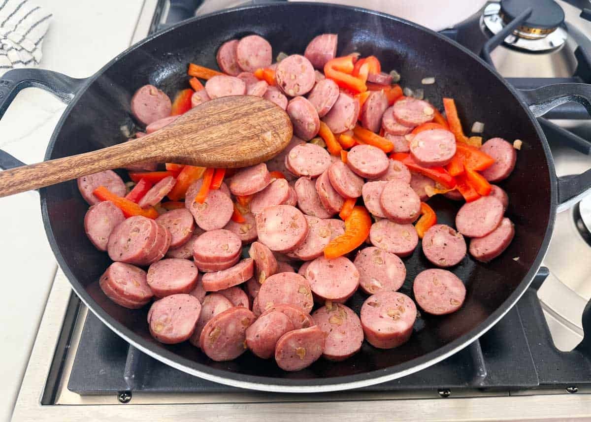 This sausage and rice skillet is the perfect one-pan dinner for busy weeknights packed with savory sausage, rice, and tender veggies! It's a hearty meal the whole family will love. Sliced sausage and red bell peppers sautéing in a skillet as the first step of sausage and rice skillet recipe.