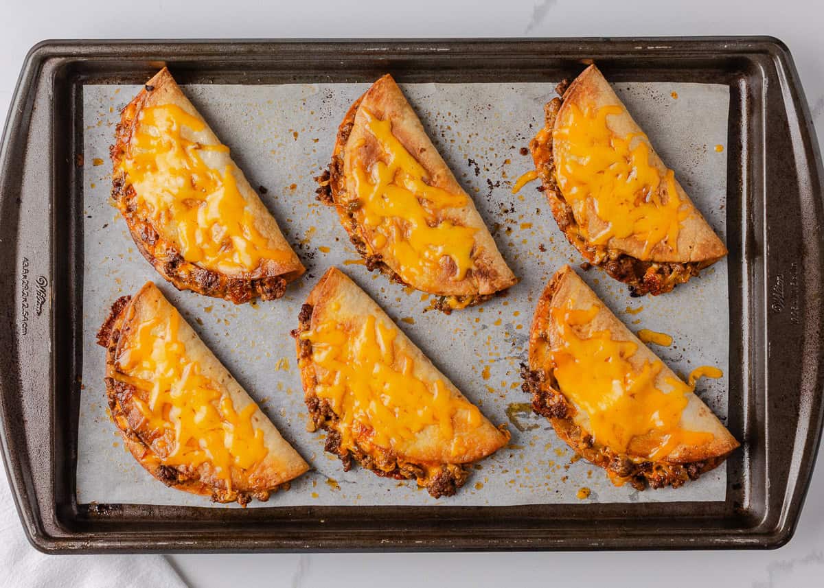 Six crispy sheet pan tacos arranged on a parchment-lined baking sheet.
