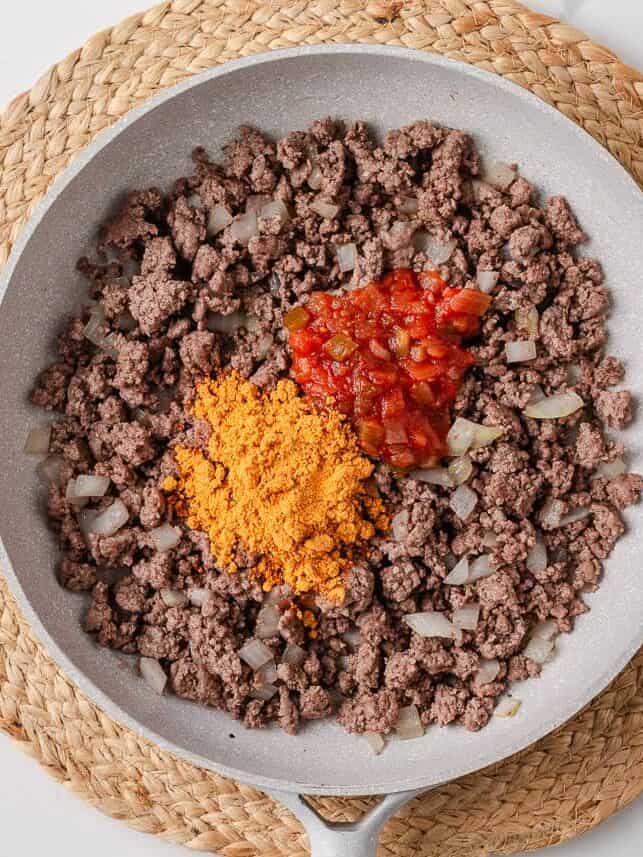 Ground beef, diced onion, taco seasoning, and salsa in a skillet before mixing.
