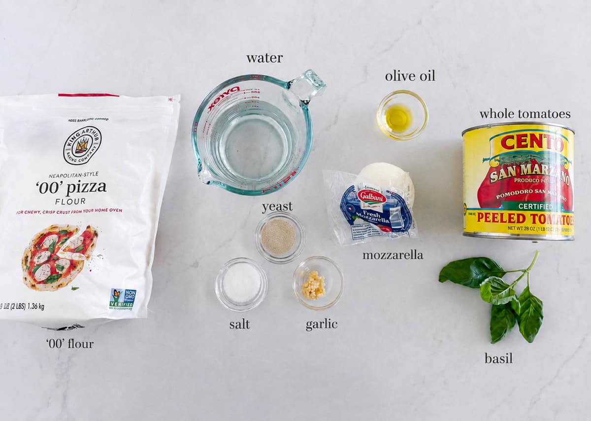 This homemade margherita pizza has a chewy crust, melted mozzarella, and fresh tomato and basil on top. A classic Italian favorite with simple, fresh flavors. Margherita pizza ingredients on the counter.