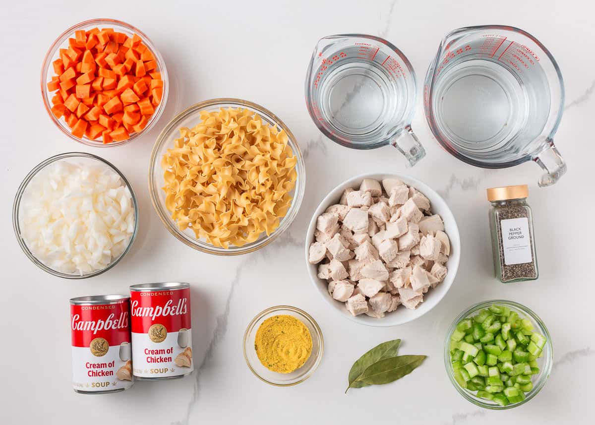 A creamy twist on a classic soup, this easy-to-make creamy chicken noodle soup is exactly what you need when you're curled up under a blanket this winter! Ingredients for creamy chicken noodle soup including diced carrots, celery, onions, egg noodles, cooked chicken, cream of chicken soup, broth, bay leaf, and seasonings.