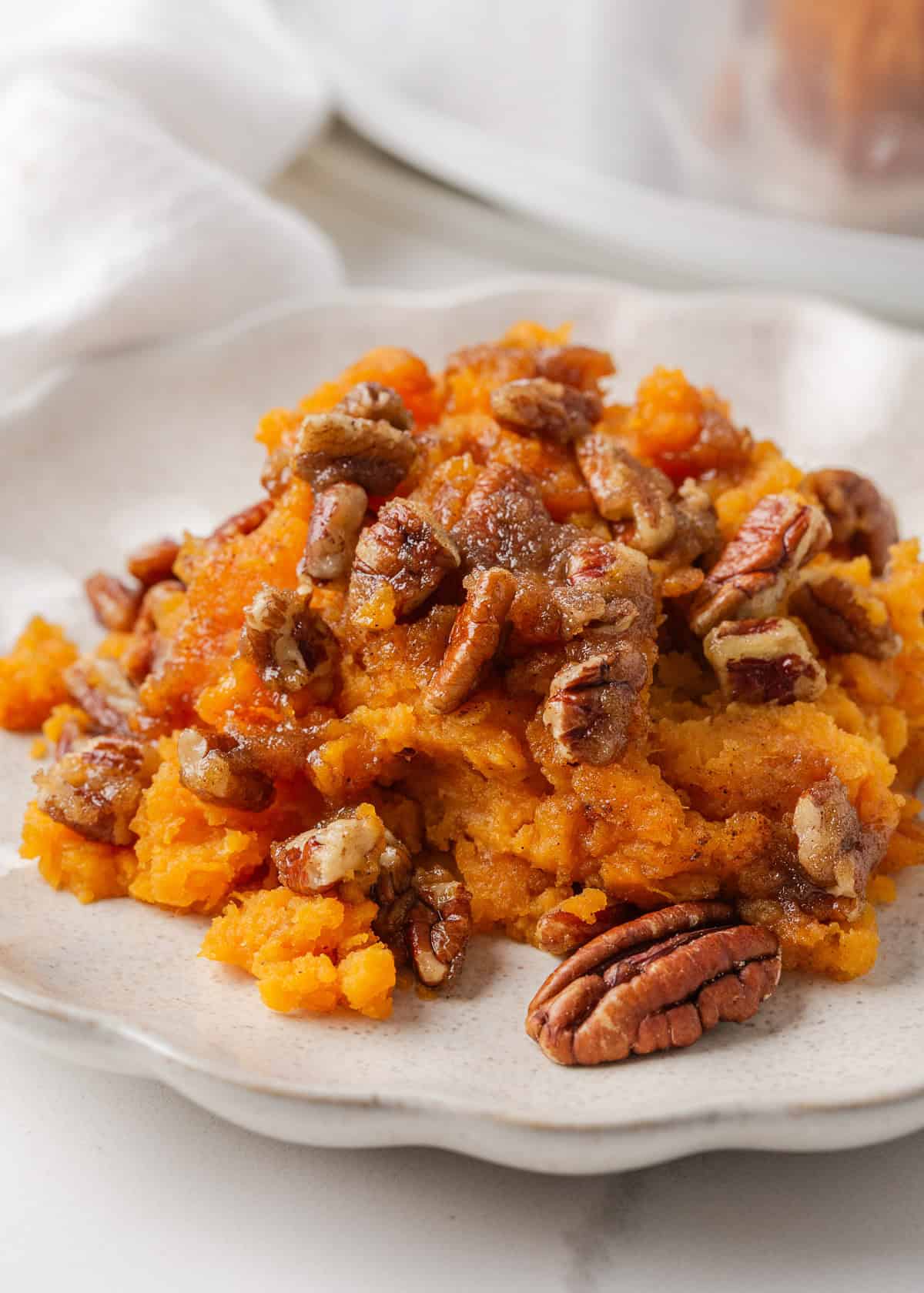 Crockpot sweet potato casserole makes holiday cooking easy. With creamy mashed sweet potatoes and a crunchy pecan topping, it's a holiday side dish not to be missed! Crockpot sweet potato casserole topped with candied pecans served on a white plate.