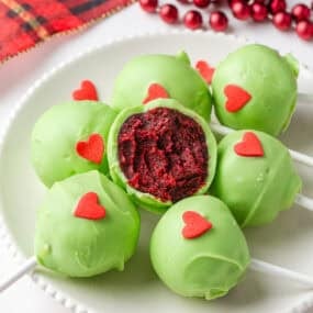 Finished Grinch cake pops with red velvet centers coated in green chocolate and topped with red hearts.