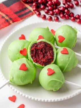 Finished Grinch cake pops with red velvet centers coated in green chocolate and topped with red hearts.