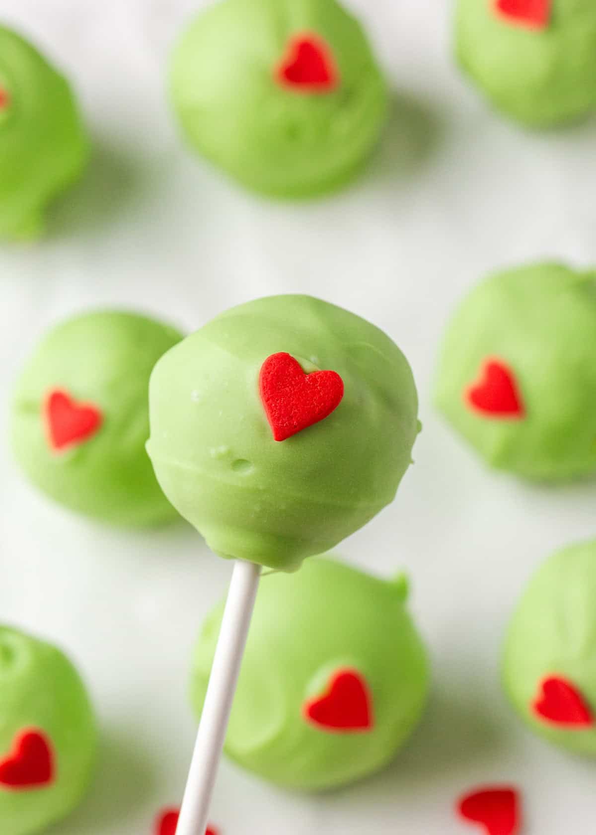 Grinch cake pops are made with moist red velvet cake and decorated with green candy coating and a little red heart. A festive Christmas dessert inspired by the classic movie! Grinch themed cake pop coated in green candy melts and decorated with a red heart sprinkle.
