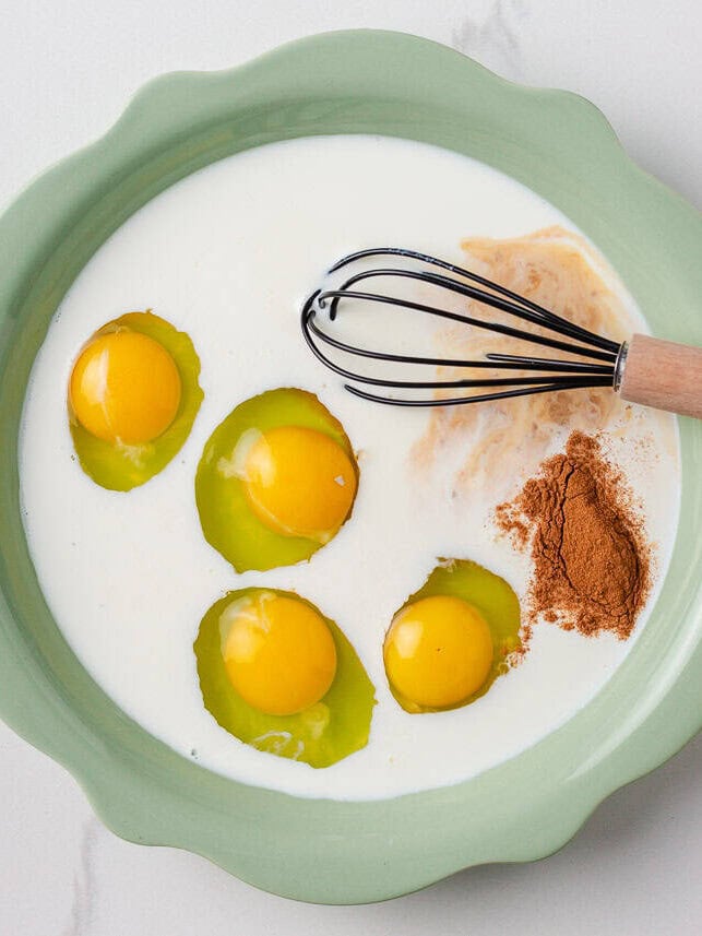 Eggs, milk, cinnamon, vanilla, and sugar in a shallow mixing dish with a whisk.