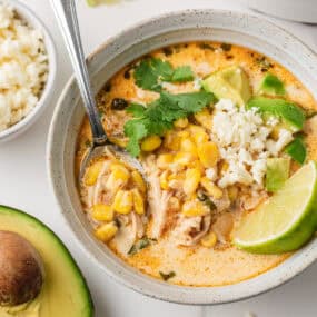 Mexican street corn soup served in a bowl with lime wedges, avocado chunks, cilantro, and crumbled queso fresco.