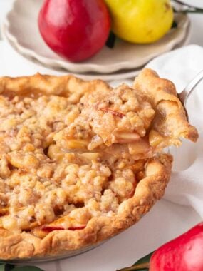 Freshly baked pear pie with golden brown crust and crumb topping, one slice being lifted to show tender spiced pear filling.