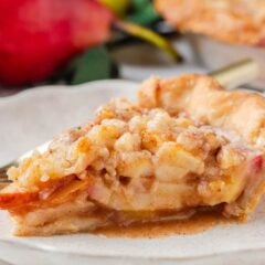 Close-up of a slice of pear pie with a flaky golden crust and cinnamon-sugar pear filling with crumble topping on a white plate.