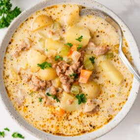 Overhead view of a bowl of creamy sausage and potato soup garnished with parsley, showing diced vegetables, sausage, and potatoes in a golden broth.