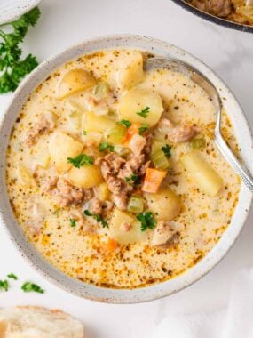Overhead view of a bowl of creamy sausage and potato soup garnished with parsley, showing diced vegetables, sausage, and potatoes in a golden broth.