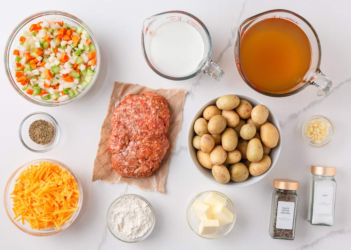 This creamy sausage potato soup is made in one pot with Italian sausage, tender potatoes, and a cheesy broth, it's a cozy way to satisfy the whole family! Flat lay of ingredients for creamy sausage potato soup, including baby potatoes, ground sausage, carrots, celery, onions, cheddar cheese, broth, half and half, garlic, and spices.