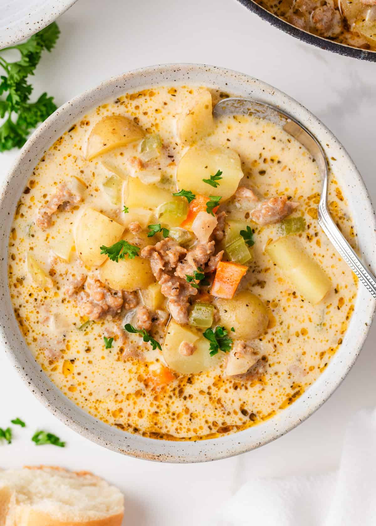 Overhead view of a bowl of creamy sausage and potato soup garnished with parsley, showing diced vegetables, sausage, and potatoes in a golden broth.