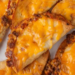 Pile of crispy sheet pan tacos with golden cheddar cheese on top.