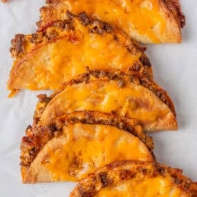 Sheet pan tacos with ground beef and melted cheese on parchment paper.