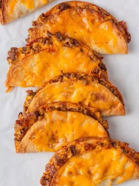 Sheet pan tacos with ground beef and melted cheese on parchment paper.