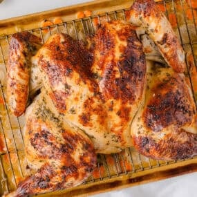 Herb butter roasted spatchcock turkey on a baking rack with carrots and onions underneath.