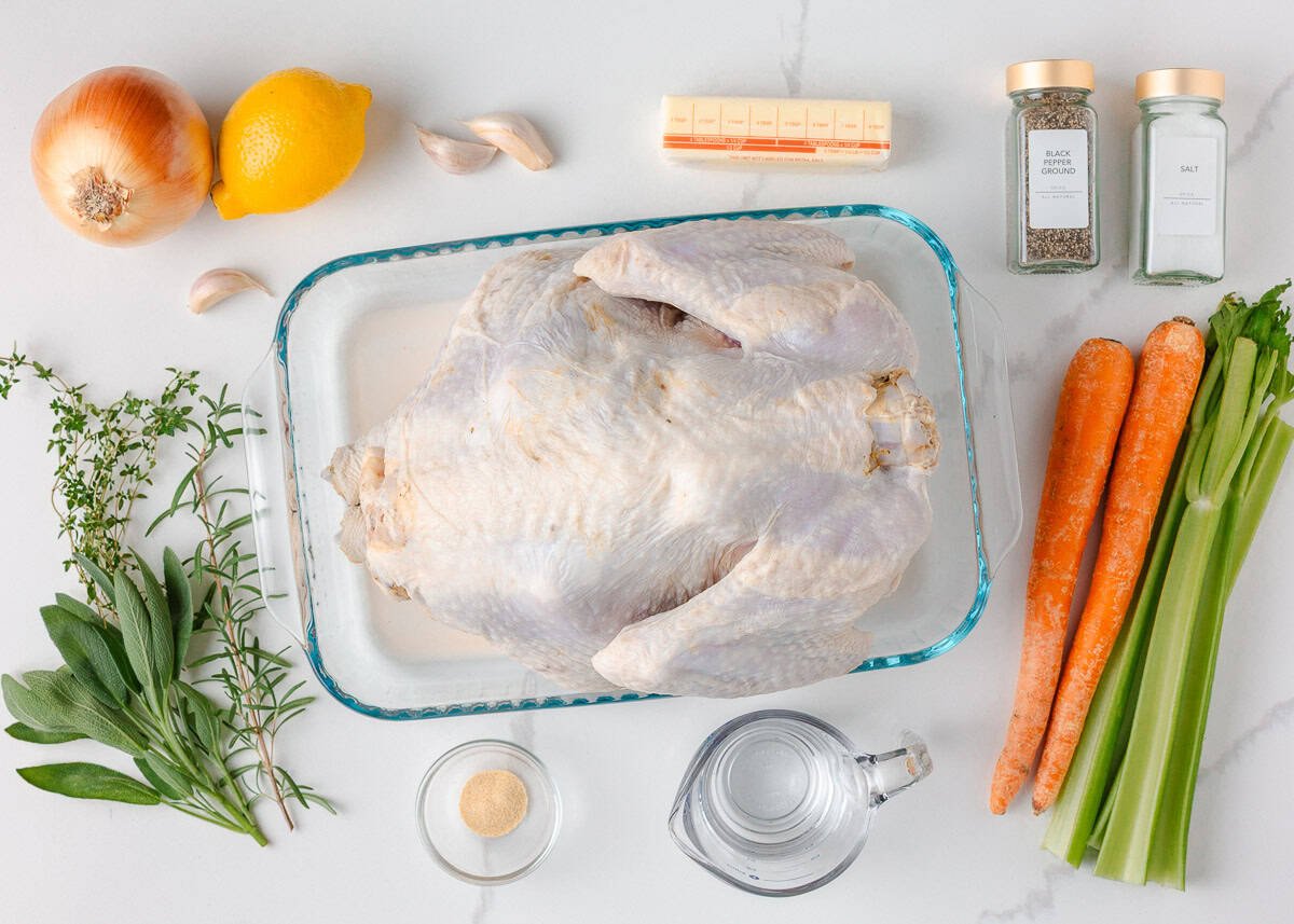 Overhead shot of raw turkey with fresh herbs, carrots, celery, onion, lemon, garlic, butter, and seasonings.
