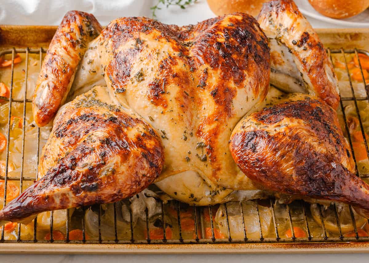 Crispy oven roasted spatchcock turkey resting on a sheet pan with vegetables.