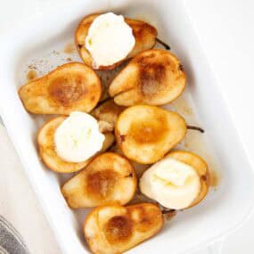 Baked pears topped with melting vanilla ice cream in a white baking dish.