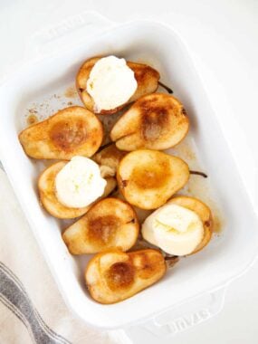 Baked pears topped with melting vanilla ice cream in a white baking dish.