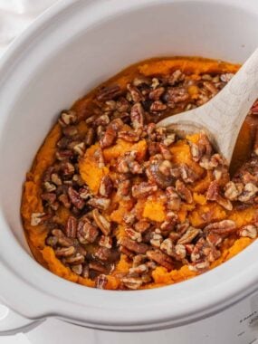 Crockpot sweet potato casserole with brown sugar pecan topping and wooden spoon.