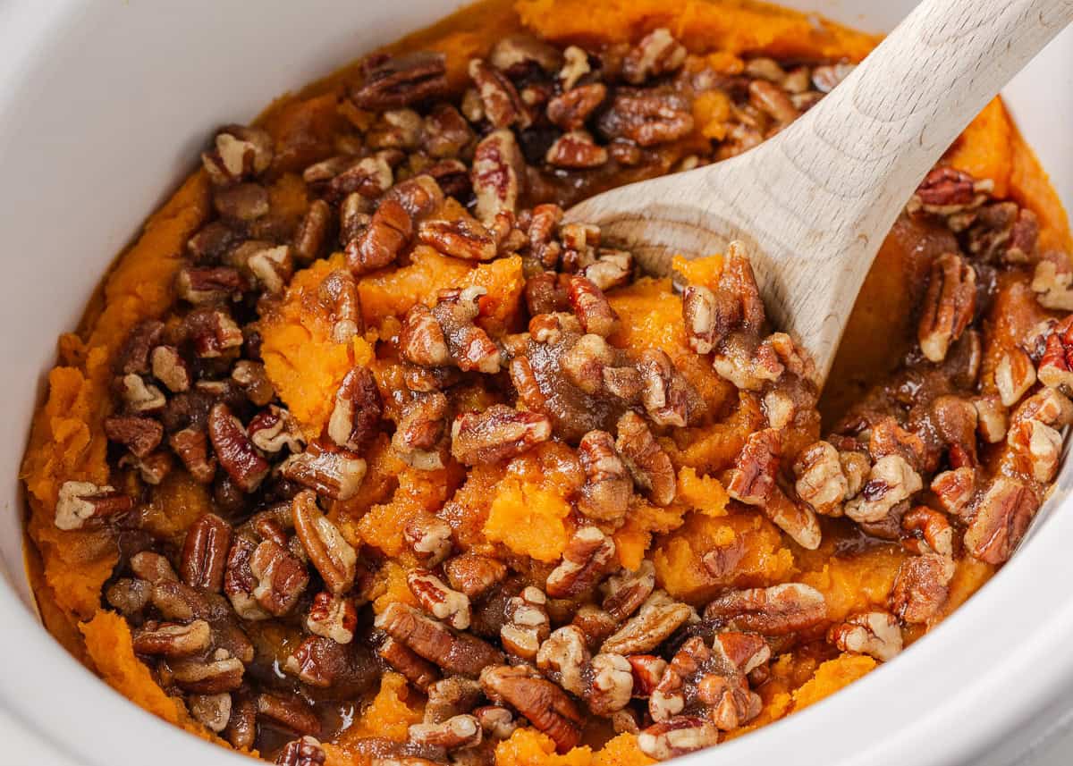 Crockpot sweet potato casserole makes holiday cooking easy. With creamy mashed sweet potatoes and a crunchy pecan topping, it's a holiday side dish not to be missed! Crockpot filled with sweet potato casserole and crunchy pecan topping.