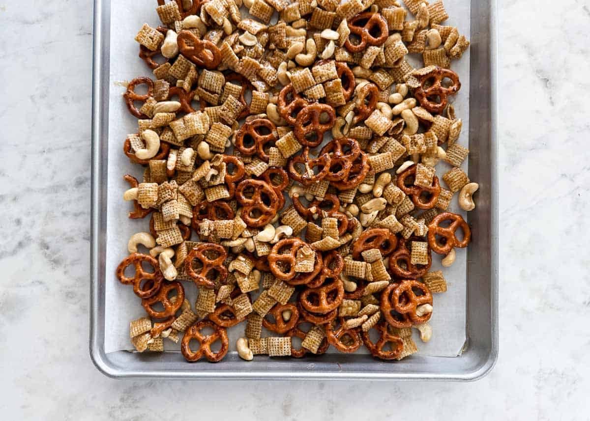 Sheet pan of fall Chex mix with pretzels, cashews, and cereal coated in a buttery brown sugar glaze before adding candy.