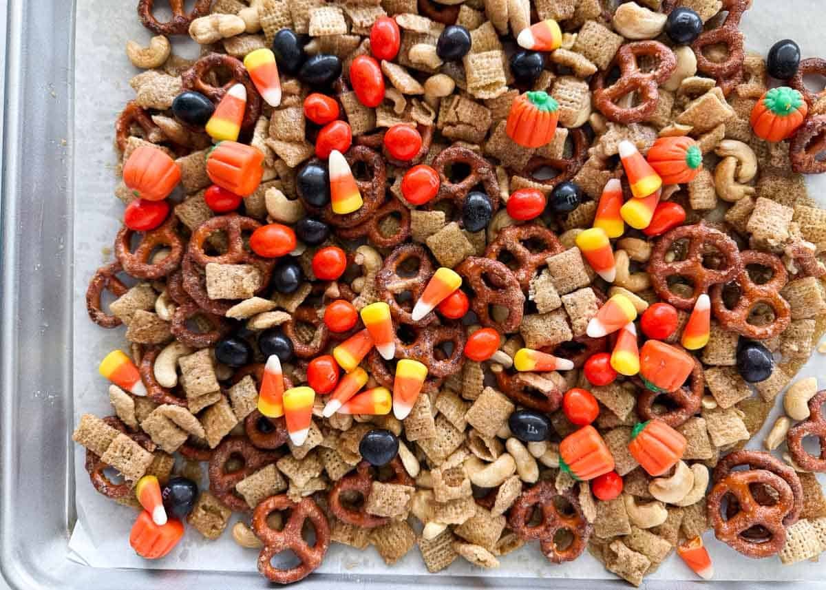 Fall Chex mix on a baking sheet with pretzels, Chex cereal, cashews, candy corn, M&M’s, and mellowcreme pumpkins.