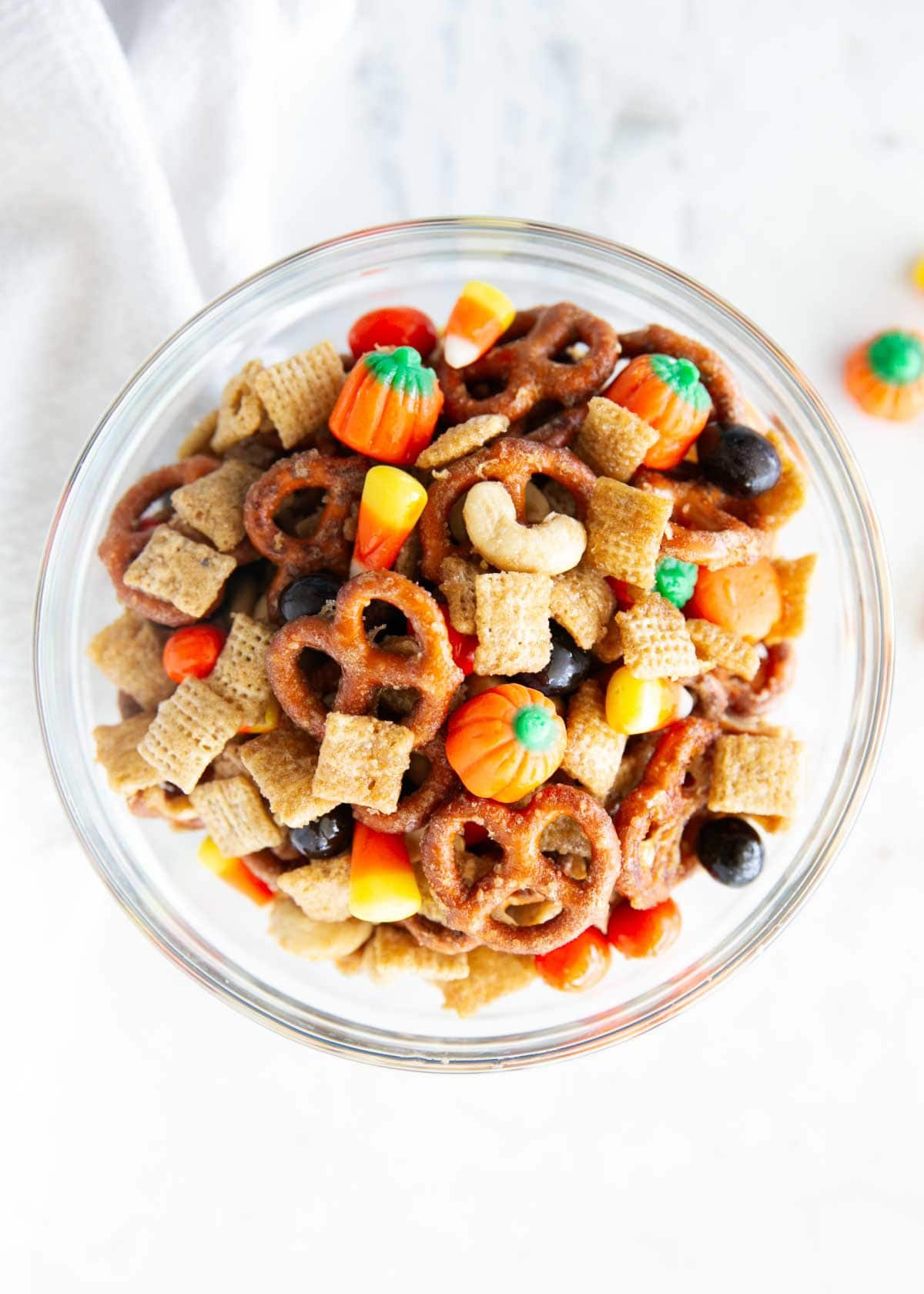 Glass bowl filled with fall snack mix with Chex, pretzels, nuts and fall candy.