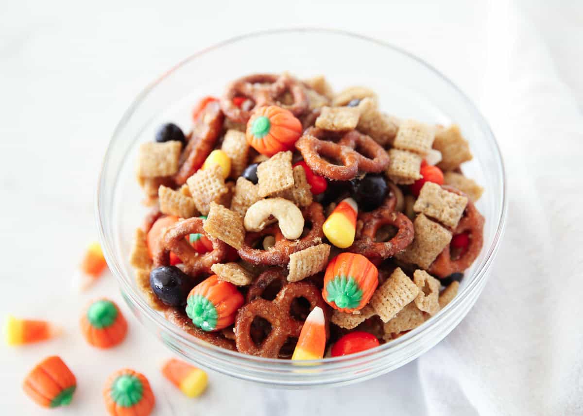 Bowl of fall Chex mix with candy corn, mellowcreme pumpkins, pretzels, and salted cashews coated in a sweet glaze.