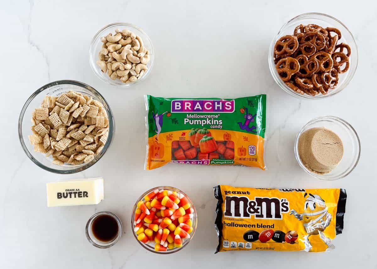 Ingredients for a fall harvest Chex mix including Chex cereal, pretzels, cashews, candy corn, and mellowcreme pumpkins.